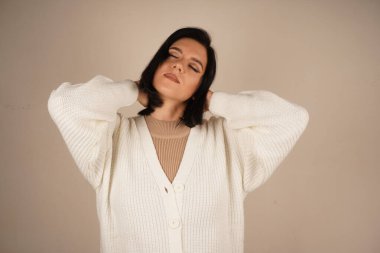 Rahat beyaz bir kazak giymiş bir kadın gözlerini nazikçe kapatır. Huzur ve sükûnet dolu güzel bir anın tadını çıkarır gibi.