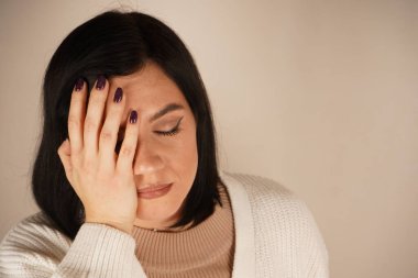 Kadın şakağına tek eliyle dokunuyor ve kötü bir baş ağrısının sinyalini veriyor. Duruşu rahatsızlığı vurguluyor. Sahne ağrı yönetimi ve rahatlama ihtiyacına odaklanıyor.