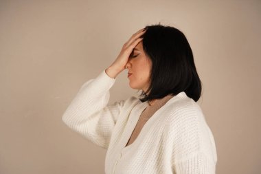 Kadın şakağına tek eliyle dokunuyor ve kötü bir baş ağrısının sinyalini veriyor. Duruşu rahatsızlığı vurguluyor. Sahne ağrı yönetimi ve rahatlama ihtiyacına odaklanıyor.