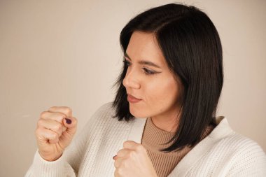 Bir kadın kollarını önünde kavuşturur, yumruklarını sıkar, korunmaya hazır olduğunun sinyalini verir. Duruşu bir savunma ve güç hissi veriyor. Jest kararlılık ve kararlılık gösteriyor.