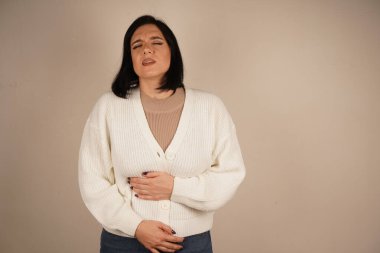 Kız ellerini karnının üstünde tutuyor, görünüşe göre rahatsız ya da acı içinde. Yüz ifadesi ve duruşu tedirginlik hissi veriyor. Bu jest fiziksel gerilimi vurgular.