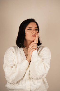 Genç bir kadın sakızını tek eliyle tutuyor, yüzünde rahatsızlık ifadesi var. Bu jest açıkça diş ağrısını ya da acıyı yansıtıyor. Sahne fiziksel bir huzursuzluğu ifade ediyor.