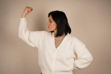 Genç bir kadın kaslarını gururla göstererek kolunu esnetiyor. Onun jesti gücü ve bağımsızlığı simgeliyor. Yüzündeki ifade güven ve güçlenmeyi yansıtıyor.