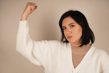 Genç bir kadın kaslarını gururla göstererek kolunu esnetiyor. Onun jesti gücü ve bağımsızlığı simgeliyor. Yüzündeki ifade güven ve güçlenmeyi yansıtıyor.