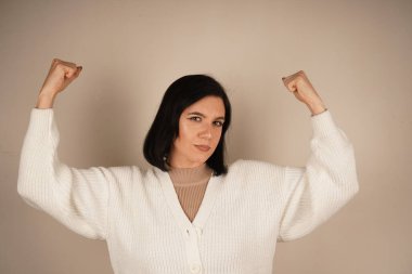 Genç bir kadın kaslarını gururla göstererek kolunu esnetiyor. Onun jesti gücü ve bağımsızlığı simgeliyor. Yüzündeki ifade güven ve güçlenmeyi yansıtıyor.