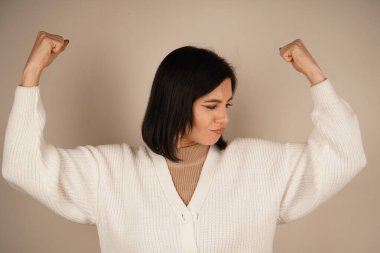 Genç bir kadın kaslarını gururla göstererek kolunu esnetiyor. Onun jesti gücü ve bağımsızlığı simgeliyor. Yüzündeki ifade güven ve güçlenmeyi yansıtıyor.