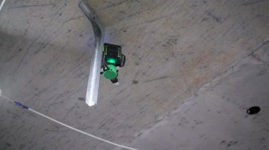 Tamamlanmamış tuğla duvarları olan küçük yeşil bir lazer seviyesi bitmemiş bir odada duruyor.