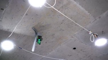 A professional laser level, set up on uneven concrete framed by the unfinished walls of an unfinished interior