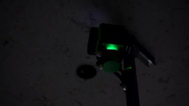 A professional laser level, set up on uneven concrete framed by the unfinished walls of an unfinished interior
