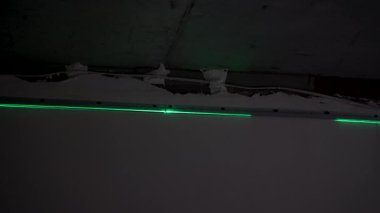 Unfinished walls and exposed beams surround the green laser level, creating sharp lines on the ceiling