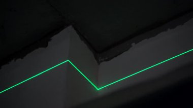 Unfinished walls and exposed beams surround the green laser level, creating sharp lines on the ceiling