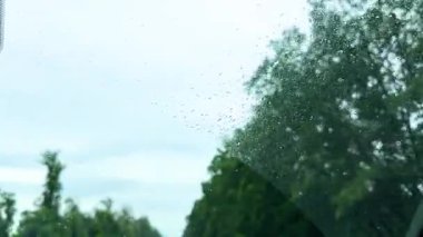 Arabanın camında yağmur damlaları dikiz aynasına odaklanmış, dışarıda fırtınalı bir atmosfer, yağmurlu yolculuk konsepti, kötü hava koşullarında araç güvenliği. Yan ayna yağmurlu araba penceresinden geçen yolu yansıtıyor, bulutlu gökyüzünü.