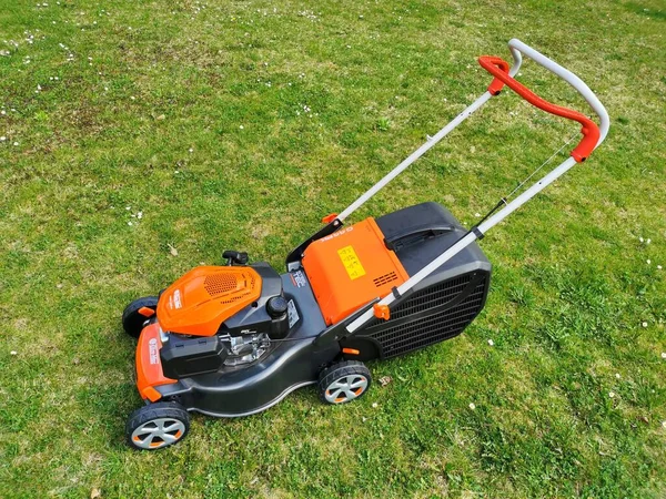 stock image Motorized petrol garden lawnmower, orange-black color, standing on the lawn, view from the left, image