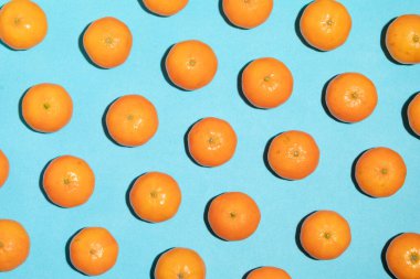 Sulu ve sağlıklı mandalinalar, düzensiz şekilli, mavi bir arkaplan üzerine dizilmiş, pop sanat tarzı bir görüntü ve doku oluşturuyorlar.