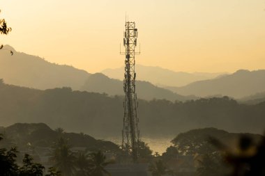 Bir telekomünikasyon anteni gün batımında, Luang Prabang, Laos 'tan gelen açık bir sisin ortasında, dağların arasında duruyor.