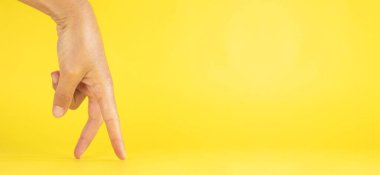 A woman's hand, imitating legs with fingers, humorously, like walking upright, on a yellow background