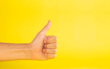 A woman's hand, with thumb up finger, making a gesture of like, or ok, on a yellow background