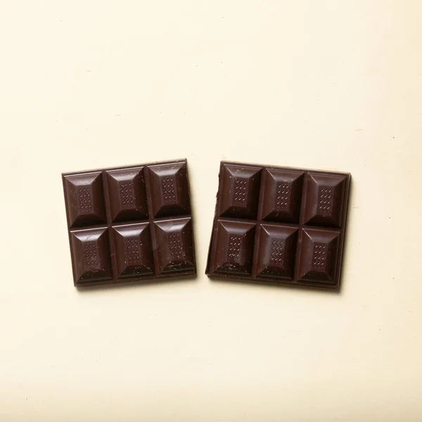 Halved dark chocolate bar, cocoa, handmade and nutritious without additives, on beige smooth background. Studio shot