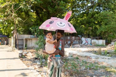 Yangon, Myanmar - 19 Aralık 2019: Genç bir adam kucağında küçük kızıyla yürür, kendini pembe bir şemsiyeyle Yangon, Burma, Myanmar 'da güneşten korur.