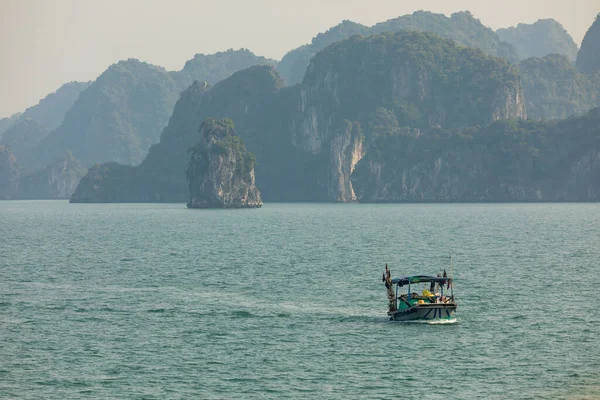 Denizde yalnız bir balıkçı teknesi, Vietnam, Güneydoğu Asya 'daki Ha Long Körfezi' ndeki dağların ve adaların karst arazisinde batmış.