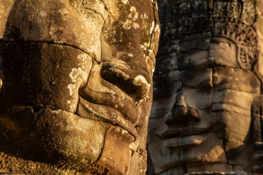 İki taş surat, Bayon Tapınağı 'nda yontulmuş, akşam güneşinin son ışıklarıyla aydınlanmış, Angkor, Kamboçya.