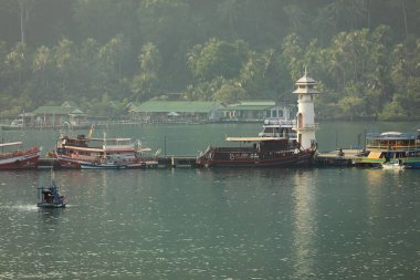 Tayland Körfezi 'ndeki Koh Chang adasında, yağmur ormanlarıyla çevrili küçük bir körfezde bir deniz feneri ve bir grup tekne.