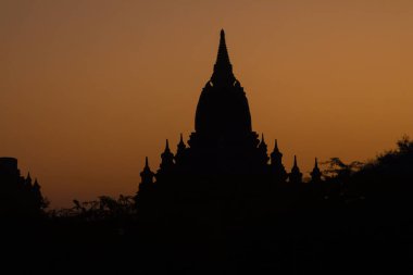 Bagan, Myanmar tapınaklarından birinin silueti, hava kararmadan önce turuncu gökyüzüne karşı.