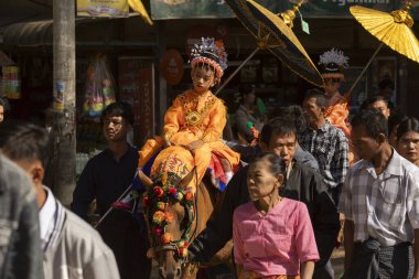 Bagan, Myanmar - 25 Aralık 2019: Geleneksel kıyafetler giymiş küçük bir kız, Theravada Budizmi geleneğine göre Shinbyu sırasında ata biniyor.