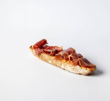 A toast of bread with olive oil and natural tomato, with cured serrano ham iberico, on a white background clipart