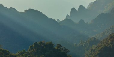 Gün batımında güneş ışınlarıyla geçilen yağmur ormanlarıyla kaplı dağların Laosland manzarası, Vang Vieng, Laos, Güneydoğu Asya