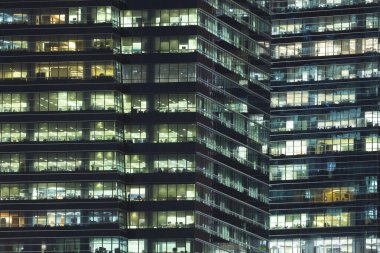 Geceleri aydınlatılmış çelik ve cam gökdelen binalar, evler ve ofisler.