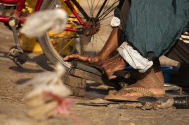 Yaşlı bir adam, Pakse 'deki Bai Don pazarında elinde bir değirmen taşıyla bıçak ve pala keskinleştiriyor.