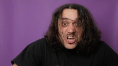 Genç yakışıklı serseri uzun saçlarını sallıyor ve keçi işaretini gösteriyor. Genç serseri saçlarını müziğin ritmine göre sallar ve zevkini gösterir. Yüksek kalite 4k görüntü