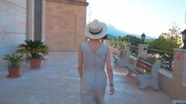  Genç çekici bir kız cadde boyunca yürür. Beyaz şapkalı genç bir kız cadde boyunca yürüyüp güzel bir manzaranın tadını çıkarıyor..
