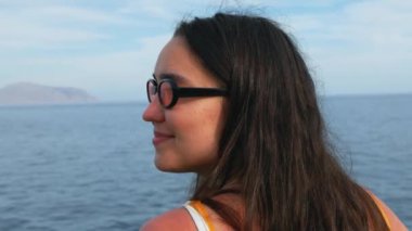 Genç ve çekici bir kız kameraya bakar ve mavi okyanusun arka planına gülümser. Genç milenyum kızı denizde harika bir tatil yapıyor.. 