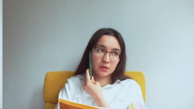 Genç ve çekici bir iş kadını telefonda konuşur ve belgelere bakar. Yüksek kaliteli FullHD görüntüler