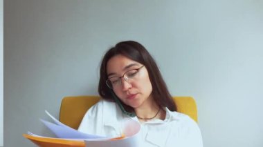 Genç ve çekici bir iş kadını telefonda konuşur ve belgelere bakar. Yüksek kaliteli FullHD görüntüler