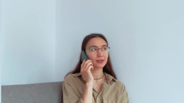 Genç ve çekici bir kız oturma odasında otururken cep telefonuyla konuşuyor. Yüksek kalite 4k görüntü