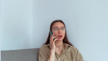 Genç ve çekici bir kız oturma odasında otururken cep telefonuyla konuşuyor. Yüksek kalite 4k görüntü