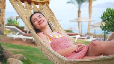 Genç ve çekici bir kız palmiye ağaçlarının gölgesinde bir hamakta dinleniyor. Yüksek kalite 4k görüntü