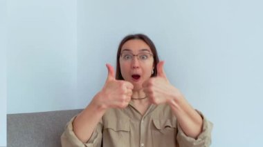 Genç ve çekici bir kız şaşırdı ve baş parmağını kaldırdı. Yüksek kalite 4K görüntü.