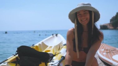 Genç çekici kız turist bir kanoya oturur. Çekici kız denizde kano yapıyor..