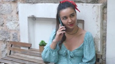Kafedeki masada oturan genç ve çekici bir kız cep telefonuyla konuşuyor. Güzel genç bir kadın akıllı telefonuyla erkek arkadaşıyla konuşuyor..