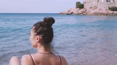 Muhteşem bir deniz manzarasının arka planında poz veren manken. Güzel genç kız kumsalda güneşleniyor ve denizde tatilinin tadını çıkarıyor..