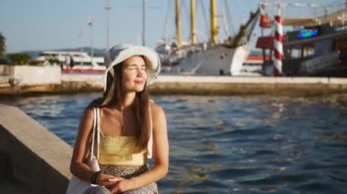 Hasır şapkalı çekici genç bir kadın kıyıda oturur ve uzaklığa bakar. Genç bir kız, elini güneşten koruyarak uzaklığa bakar..