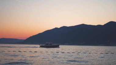 Arka planda güzel bir günbatımı olan sakin bir denizde yelken açan bir tekne. Gökyüzü sıcak renklerle boyanır, huzurlu ve huzurlu bir atmosfer yaratır. Yüksek kalite