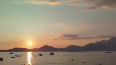 Güneş okyanusun üzerinde batıyor, suyun üzerine sıcak bir parıltı saçıyor. Gün batımında demirli teknelerle dolu bir deniz bölmesi tasasız ve sakin bir atmosfer yaratır. Yüksek kalite