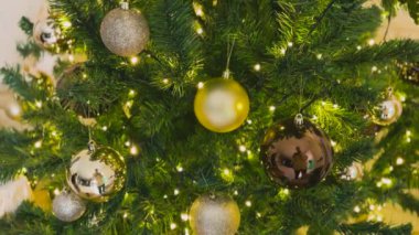 Üzerinde altın süsler ve bir fiyonk olan bir Noel ağacı. Ağaç parlıyor ve tuğla bir duvarın önünde duruyor. Yüksek kalite