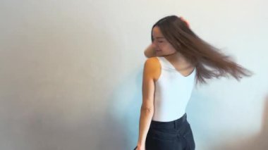 Beyaz bir duvarın önünde en sevdiği şarkıyla dans eden çekici genç bir kadın. O, beyaz bir gömlek ve siyah pantolon giyiyor. Yüksek kalite.