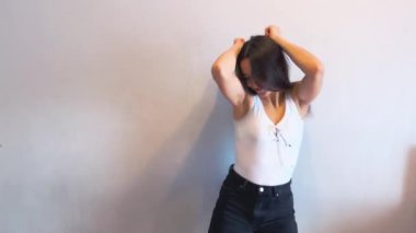 Beyaz bir duvarın önünde en sevdiği şarkıyla dans eden çekici genç bir kadın. O, beyaz bir gömlek ve siyah pantolon giyiyor. Yüksek kalite.